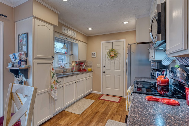 kitchen with light wood-style flooring, a sink, stainless steel microwave, dark countertops, and crown molding