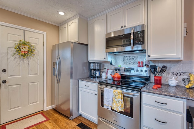 kitchen with light wood finished floors, visible vents, stainless steel appliances, white cabinetry, and backsplash