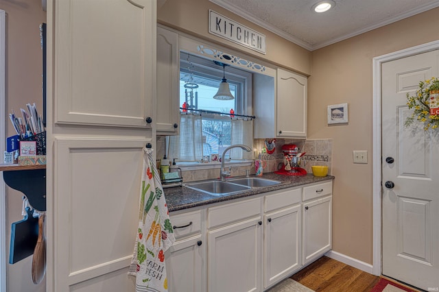 kitchen featuring dark countertops, backsplash, ornamental molding, white cabinetry, and a sink