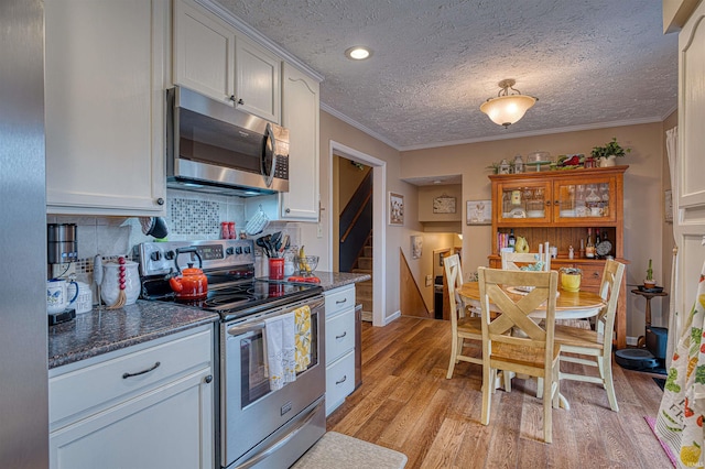 kitchen featuring white cabinetry, ornamental molding, appliances with stainless steel finishes, light wood-type flooring, and tasteful backsplash