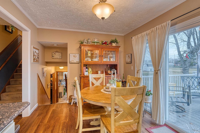 dining room featuring light wood finished floors, stairs, crown molding, and a textured ceiling