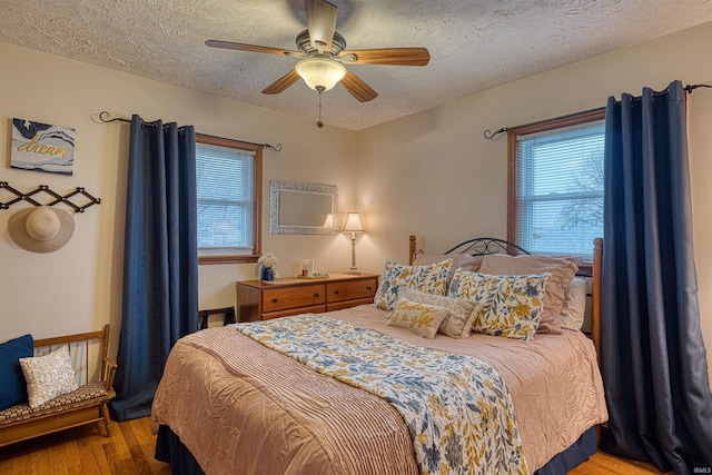 bedroom with a ceiling fan, multiple windows, a textured ceiling, and wood finished floors