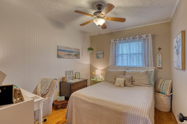 bedroom featuring ornamental molding, ceiling fan, a textured ceiling, and wood finished floors