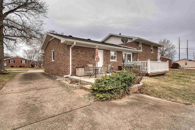 back of property with a patio area, a deck, a lawn, and brick siding