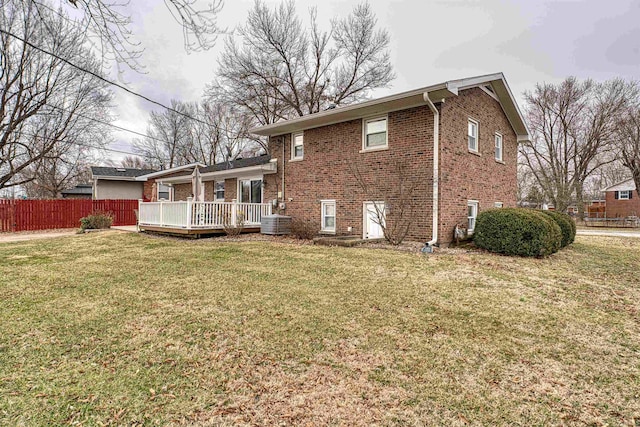 back of house with brick siding, a yard, central air condition unit, fence, and a deck