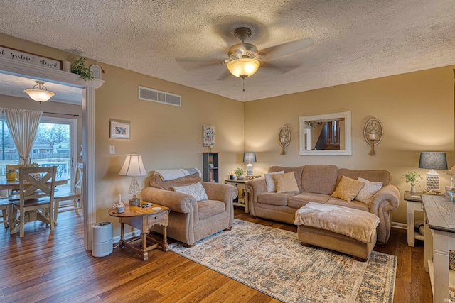 living room featuring wood-type flooring, a textured ceiling, visible vents, and a ceiling fan