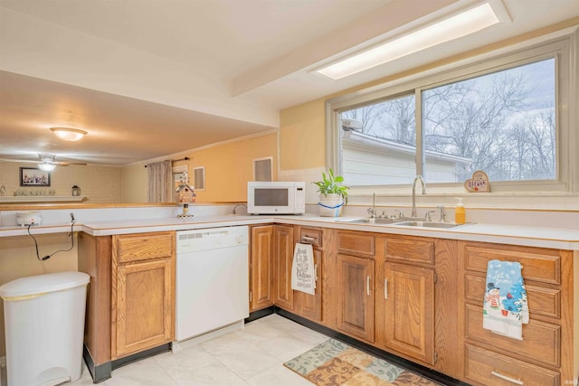 kitchen with white appliances, brown cabinetry, a peninsula, light countertops, and a sink