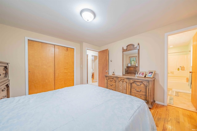 bedroom with light wood-type flooring, a closet, baseboards, and ensuite bath