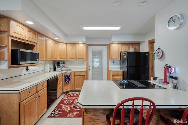 kitchen featuring black appliances, a peninsula, a sink, and light countertops