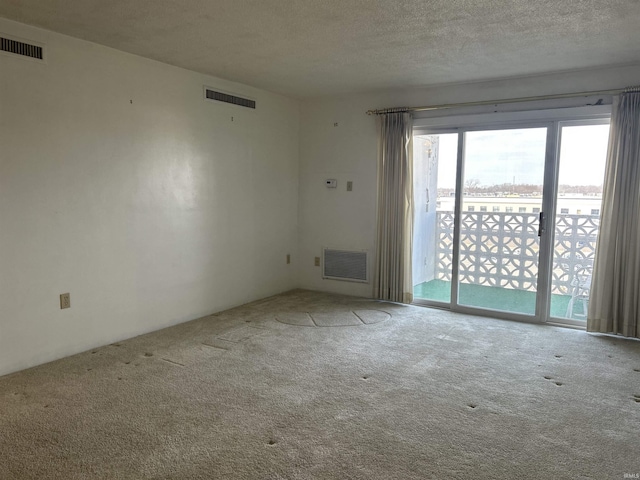 carpeted empty room featuring a textured ceiling and visible vents