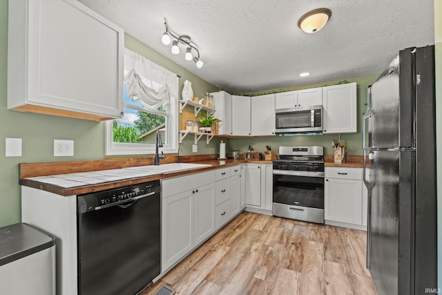 kitchen featuring light wood-style floors, white cabinets, a sink, and black appliances