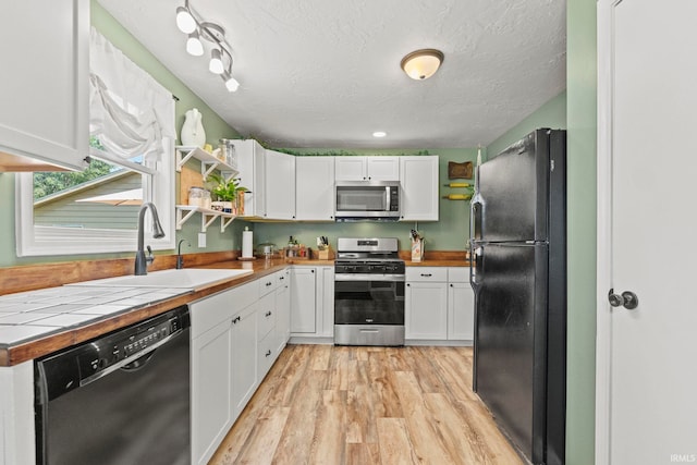 kitchen with a textured ceiling, a sink, white cabinetry, black appliances, and light wood finished floors