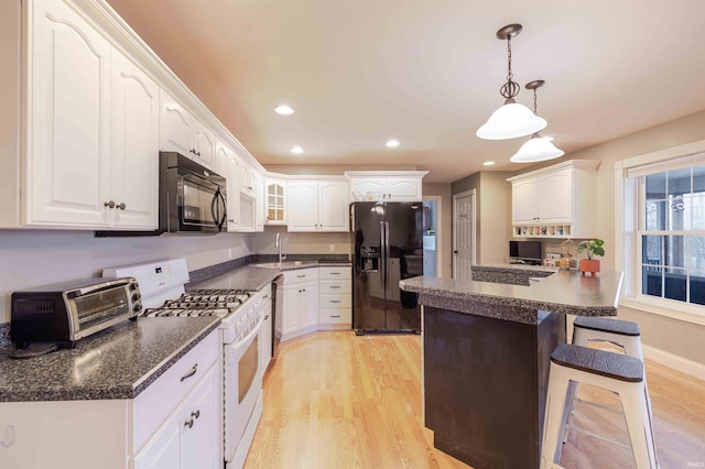 kitchen with black appliances, a breakfast bar area, dark countertops, and light wood-type flooring