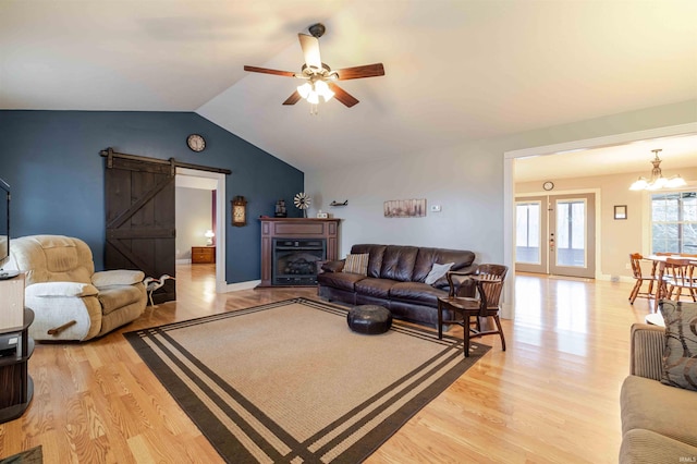 living area with lofted ceiling, a barn door, ceiling fan with notable chandelier, and light wood-style floors