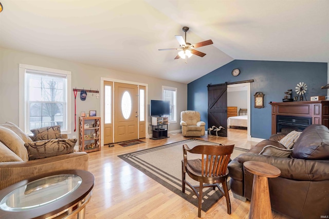 living area with lofted ceiling, light wood-style flooring, a barn door, a ceiling fan, and baseboards