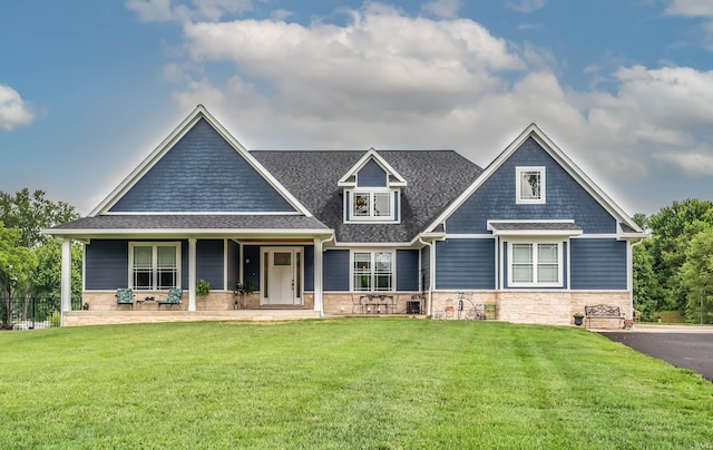 craftsman-style home with a porch, a front yard, stone siding, and roof with shingles