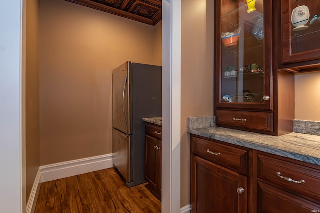 kitchen featuring dark wood-style flooring, glass insert cabinets, freestanding refrigerator, light stone countertops, and baseboards