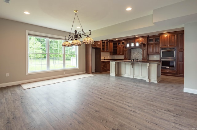 kitchen featuring recessed lighting, double oven, glass insert cabinets, open floor plan, and wood finished floors