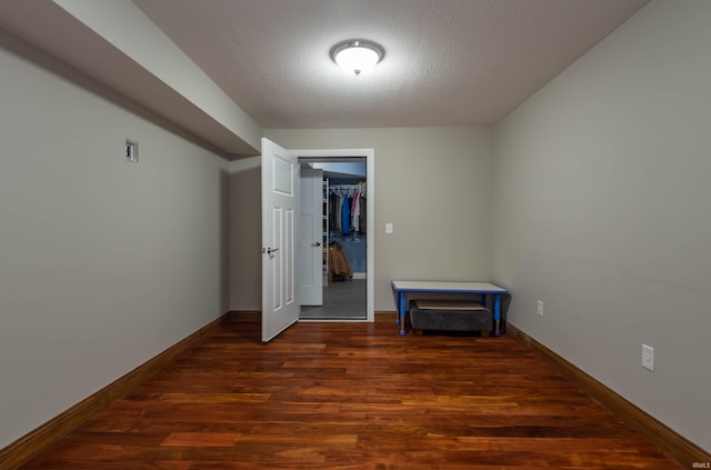 empty room featuring a textured ceiling, dark wood finished floors, and baseboards