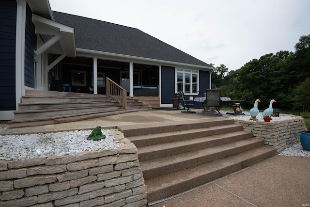 rear view of property with roof with shingles and a patio area