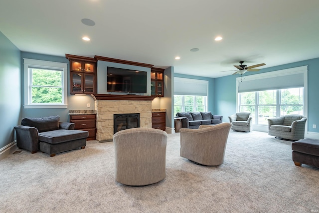 carpeted living area featuring a ceiling fan, recessed lighting, a stone fireplace, and baseboards