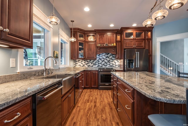 kitchen featuring light wood-style flooring, appliances with stainless steel finishes, backsplash, hanging light fixtures, and a sink