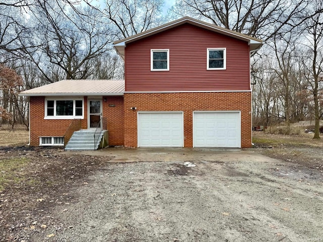 tri-level home with metal roof, driveway, brick siding, and a garage