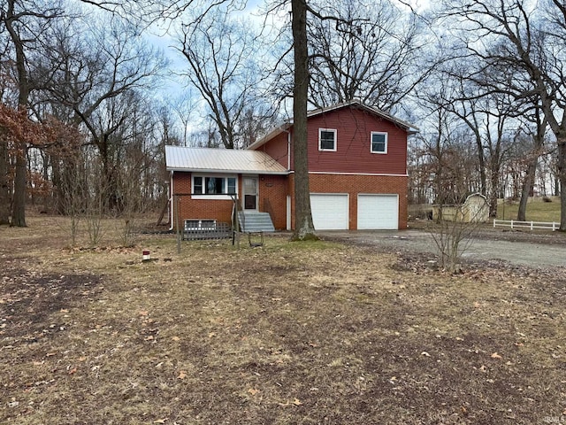 split level home featuring a garage, metal roof, brick siding, and driveway