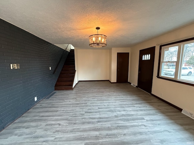 entrance foyer featuring a textured ceiling, a notable chandelier, brick wall, wood finished floors, and stairway