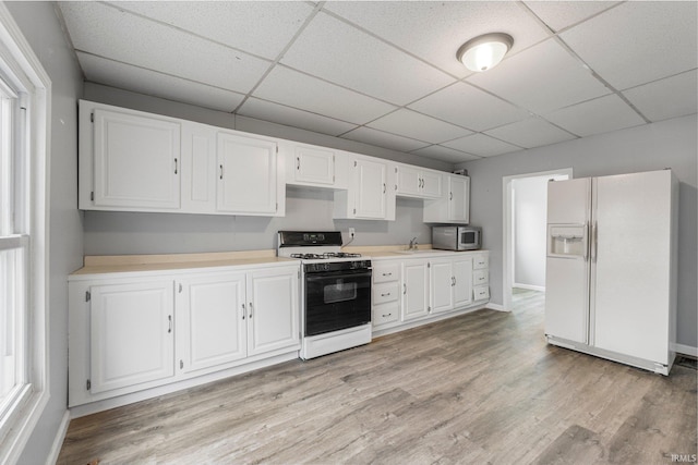 kitchen featuring white refrigerator with ice dispenser, white cabinets, light wood-type flooring, stainless steel microwave, and gas stove