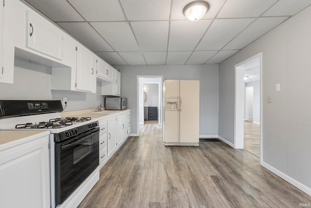 kitchen featuring range with gas stovetop, stainless steel microwave, wood finished floors, light countertops, and white fridge with ice dispenser