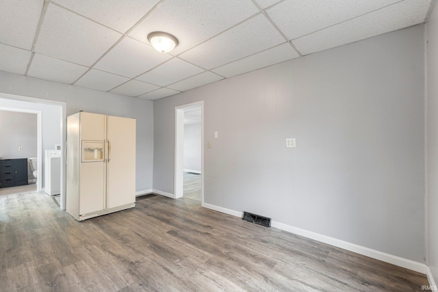 unfurnished room with baseboards, visible vents, a drop ceiling, washer / clothes dryer, and wood finished floors