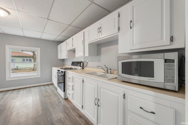 kitchen with wood finished floors, gas stove, a sink, and white cabinets