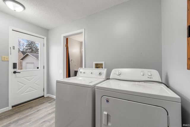 clothes washing area with washing machine and clothes dryer, light wood-style floors, a textured ceiling, laundry area, and baseboards