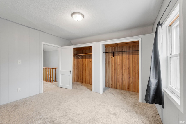 unfurnished bedroom with wooden walls, a textured ceiling, two closets, and carpet flooring