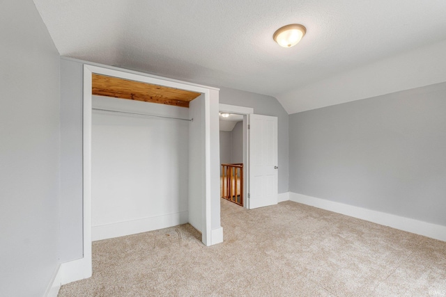 unfurnished bedroom with a textured ceiling, carpet flooring, baseboards, vaulted ceiling, and a closet