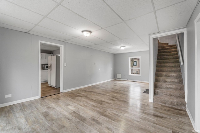 finished basement with white fridge with ice dispenser, stairway, a drop ceiling, and wood finished floors