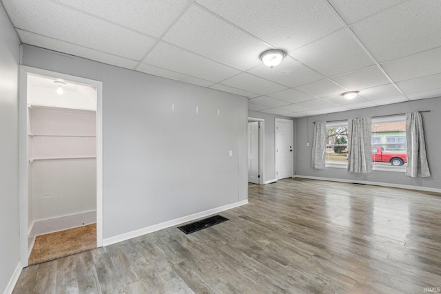 spare room featuring a paneled ceiling, visible vents, baseboards, and wood finished floors