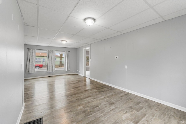 spare room with a drop ceiling, wood finished floors, visible vents, and baseboards