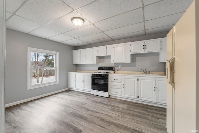 kitchen featuring white cabinets, gas range, wood finished floors, light countertops, and a sink