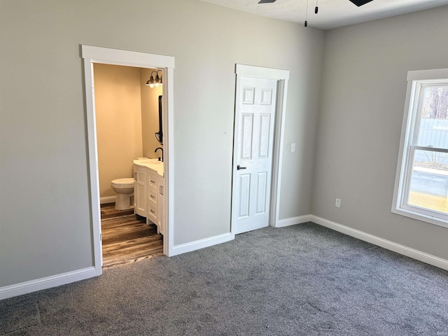 unfurnished bedroom featuring baseboards, dark carpet, a sink, and ensuite bathroom