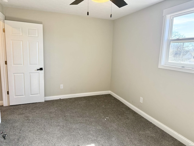 spare room with baseboards, dark colored carpet, and a ceiling fan