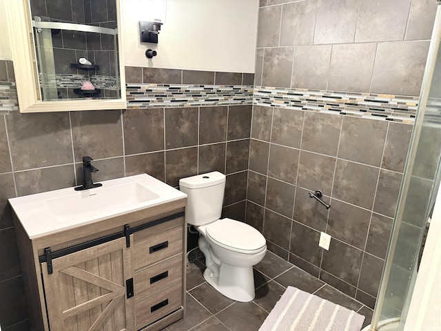 full bath with tile patterned flooring, toilet, vanity, tile walls, and a tile shower