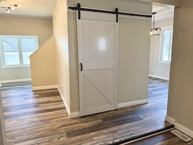 hallway with a barn door, dark wood finished floors, visible vents, and baseboards