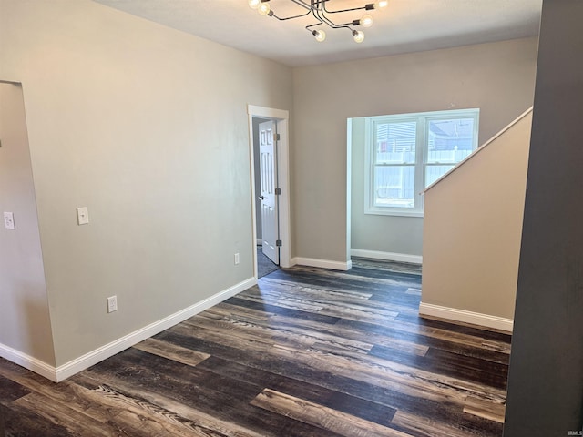 spare room featuring baseboards, a chandelier, and dark wood-type flooring