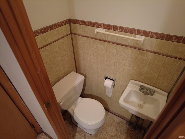 bathroom featuring a wainscoted wall, a sink, toilet, and tile walls