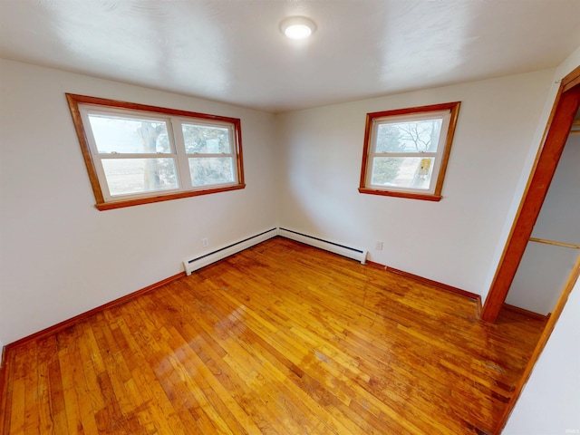 spare room featuring light wood-type flooring, a baseboard radiator, and a healthy amount of sunlight