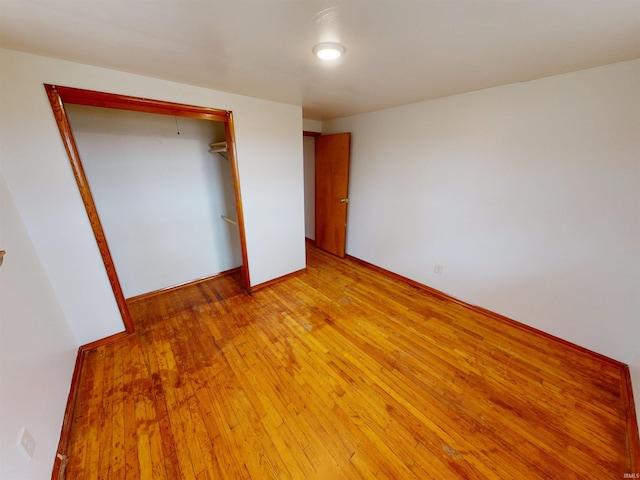 unfurnished bedroom featuring light wood finished floors, baseboards, and a closet