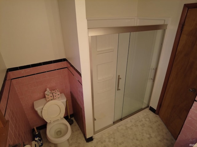 bathroom with a wainscoted wall, a stall shower, toilet, and tile walls