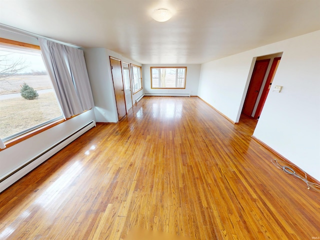 empty room featuring baseboards, a baseboard heating unit, and hardwood / wood-style floors